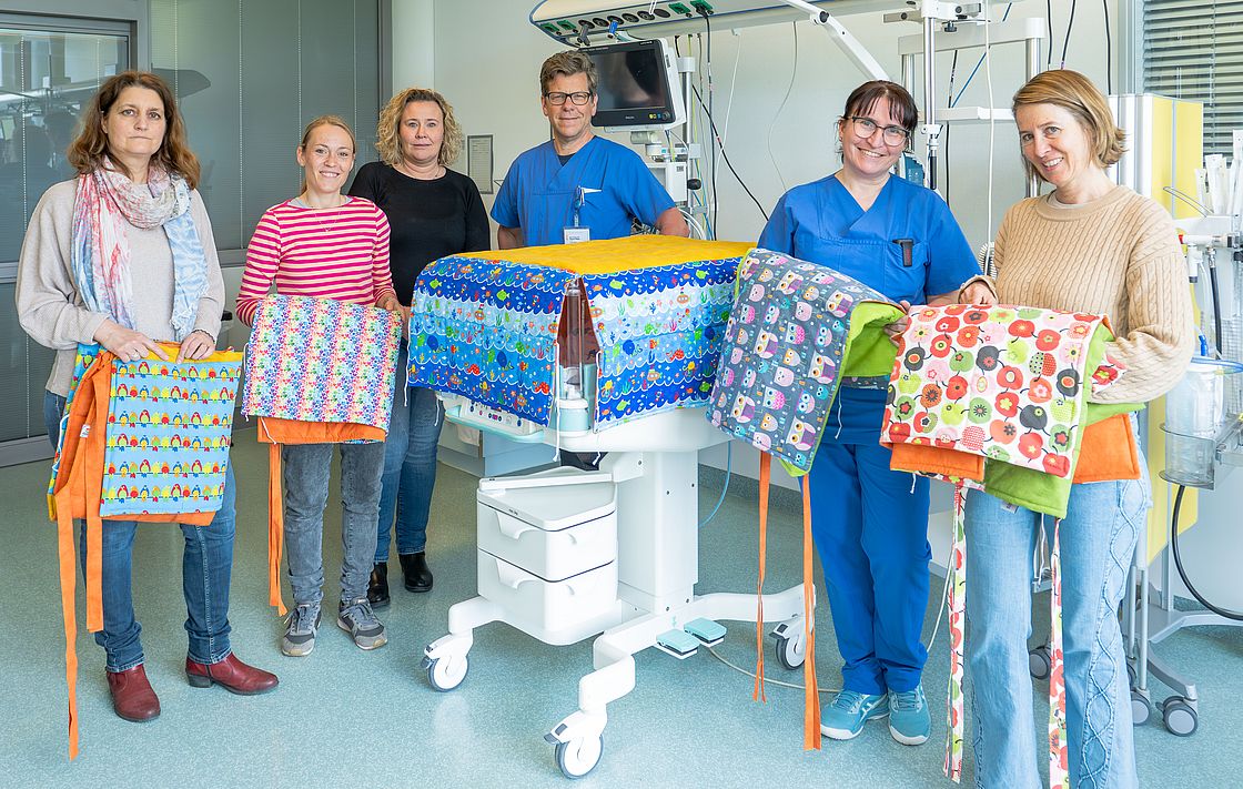 Das Bild zeigt ein Gruppenfoto, bei dem bunte, selbstgenähte Decken übergeben werden.