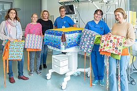 Das Bild zeigt ein Gruppenfoto, bei dem bunte, selbstgenähte Decken übergeben werden.