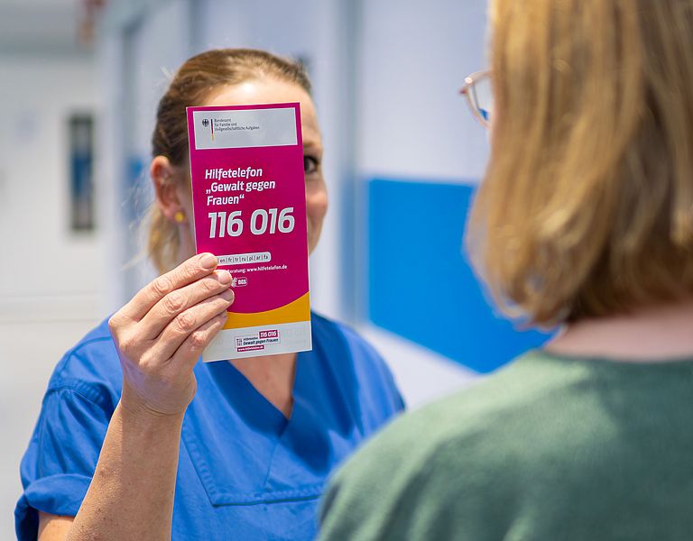 Das Bild zeigt eine Pflegekraft, die einer Patientin einen Flyer zeigt.