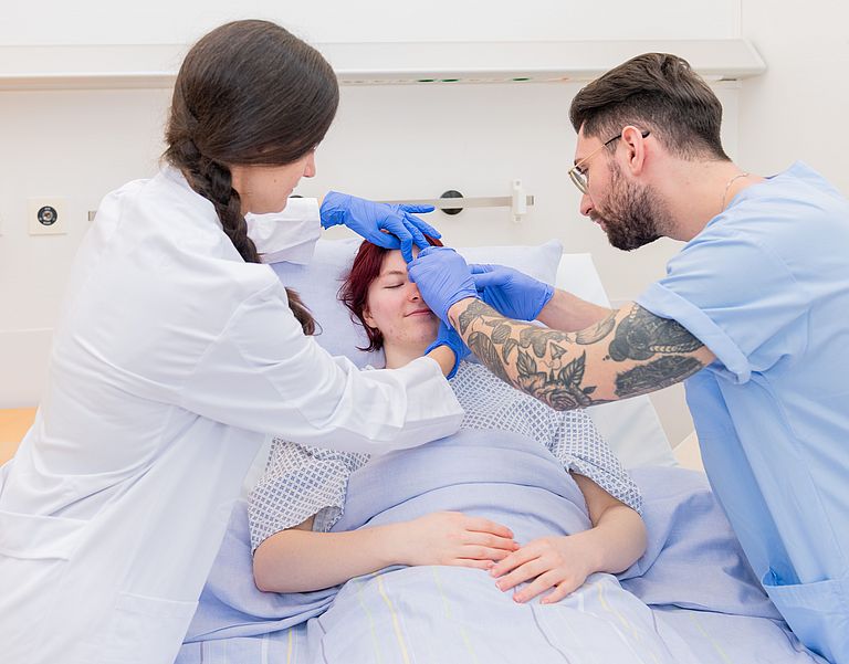 Das Bild zeigt einen Patienten mit zwei Pflegekräften.