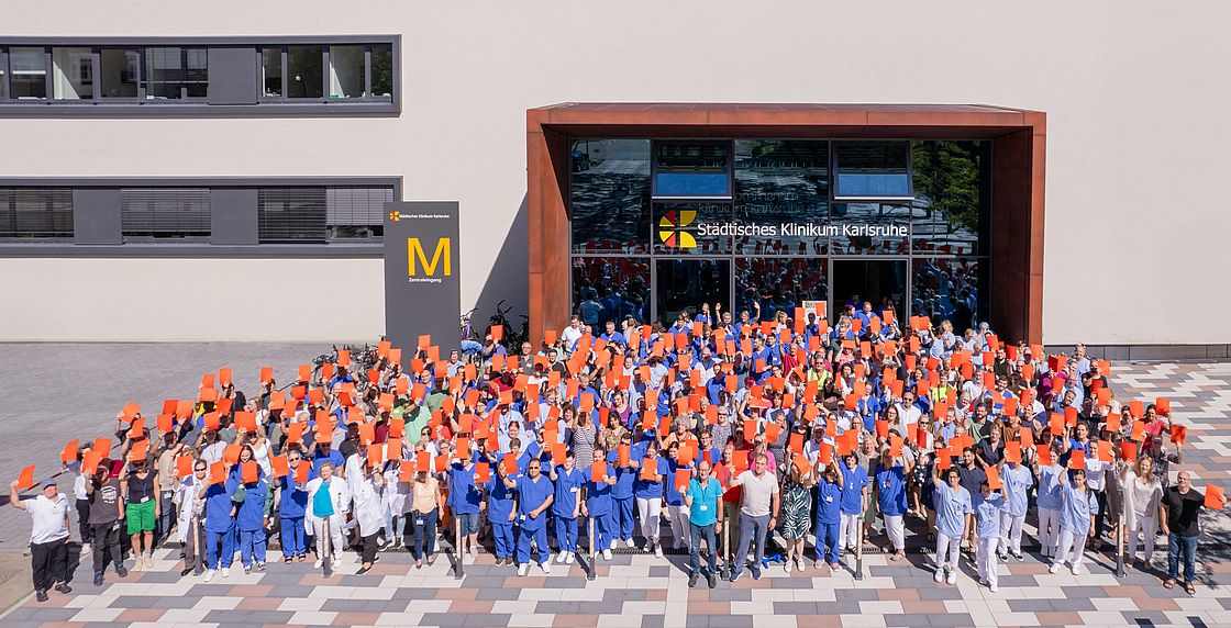 Das Bild zeigt Mitarbeitende des Klinikums Karlsruhe vor dem Gebäude mit roten Karten