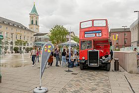 Das Bild zeigt den roten Infobus von "Herzenssache Lebenszeit" auf dem Karlsruher Marktplatz.