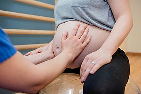 Das Bild zeigt eine Hebamme, die den Bauch einer Schwangeren abtastet.