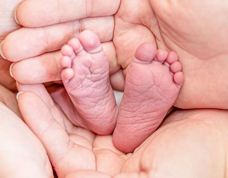 Das Bild zeigt Hände und Baby Füße, Eltern und ihr neugeborenes Kind