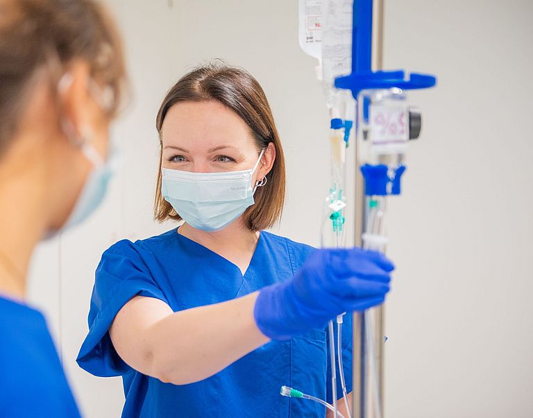 Das Bild zeigt zwei Pflegekräfte beim Richten einer Infusion