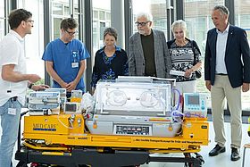 Das Bild zeigt Alexander Krauth, der Sascha Meyer (Direktor der Franz-Lust Klinik für Kinder- und Jugendmedizin), Bettina Lisbach, Bodo und Bärbel Schelling sowie Markus Heming (v.l.n.r.) die Funktionen der Fahrtrage erklärt.