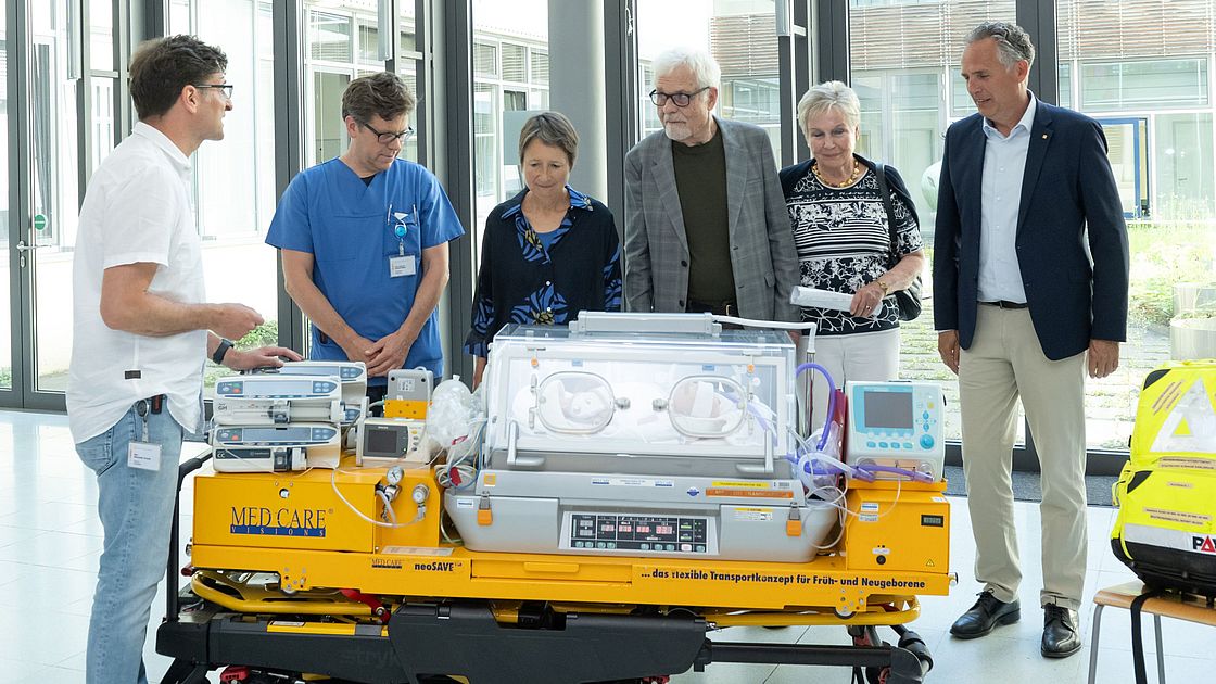 Das Bild zeigt Alexander Krauth, der Sascha Meyer (Direktor der Franz-Lust Klinik für Kinder- und Jugendmedizin), Bettina Lisbach, Bodo und Bärbel Schelling sowie Markus Heming (v.l.n.r.) die Funktionen der Fahrtrage erklärt.