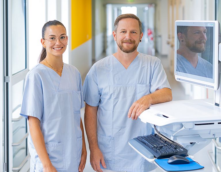 Zwei Pflegefachkräfte stehen am Patientenwagen.