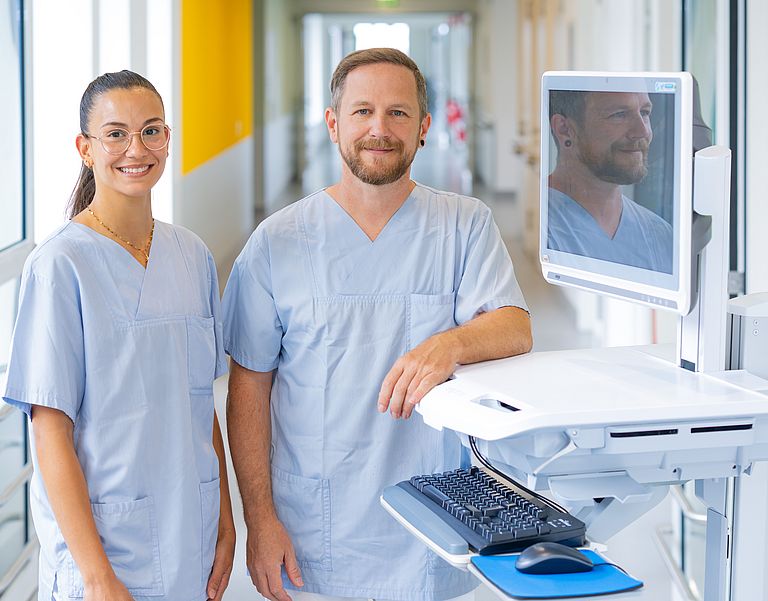 Zwei Pflegefachkräfte stehen am Patientenwagen.