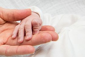 Das Bild zeigt eine Neugeborenenhand in einer Erwachsenenhand