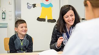 Das Bild zeigt einen kleinen Jungen und dessen Mutter im Gespräch mit einer Ärztin.