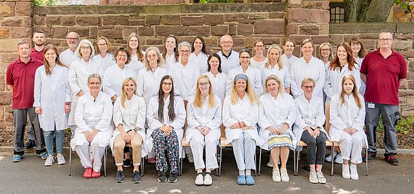 Das Bild zeigt ein Gruppenfoto des Teams der Apotheke des Städtischen Klinikums Karlsruhe. Die Personenn sind in drei Reihen aufgestellt, die erste sitzend, die anderen beiden dahinter stehend.