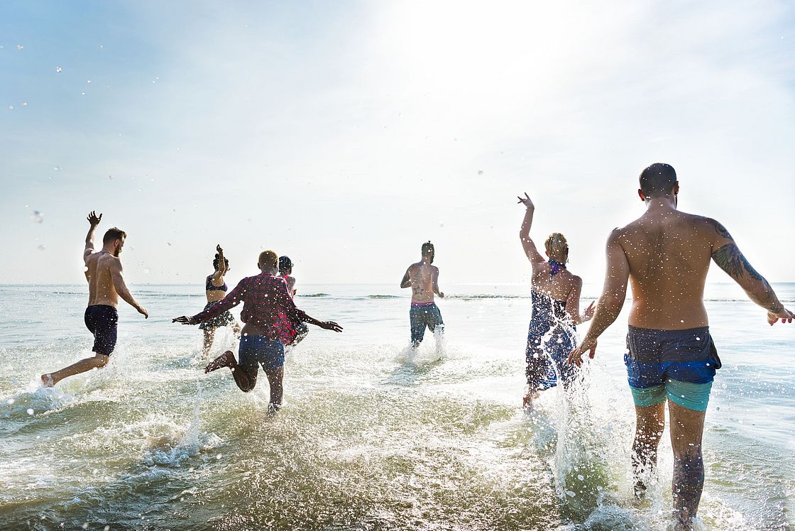 Das Bild zeigt mehrere Menschen, die ins Wasser rennen.