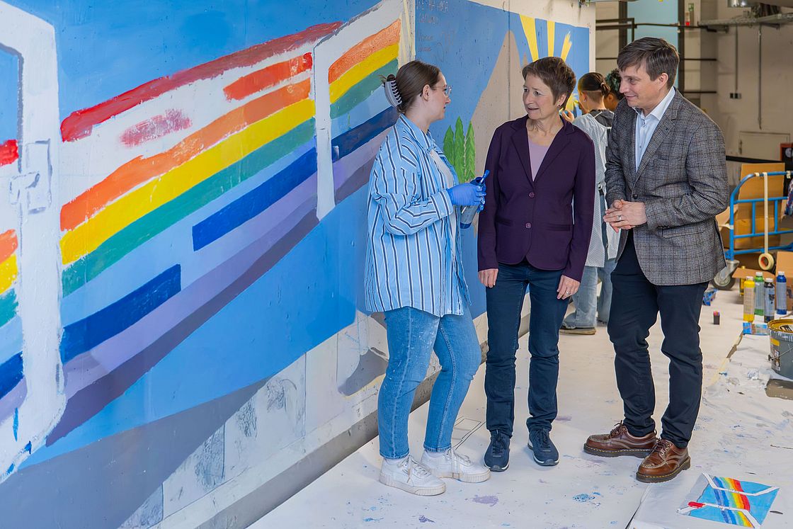 Das Bild zeigt Luisa Lehn, Lehrerin an der Drais-Gemeinschaftsschule, mit Erster Bürgermeisterin Bettina Lisbach und Prof. Dr. Dr. Martin Holderried (v.l.) vor den neu bemalten Wänden.