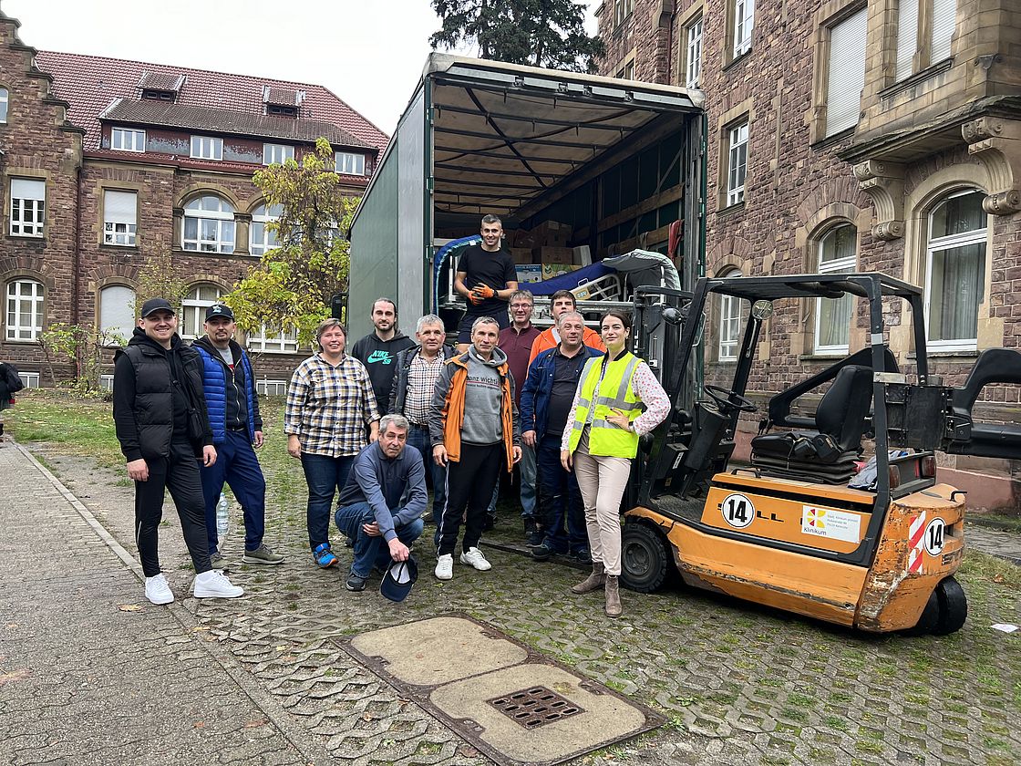 Das Bild zeigt ein Gruppenbild der Unterstützerinnen und Unterstützer der Bettenspende für die Ukraine. die Personen sehen vor dem LKW, der die Materialien in die Ukraine bringt. Im Hintergrund der Altbau Haus C des Klinikums.