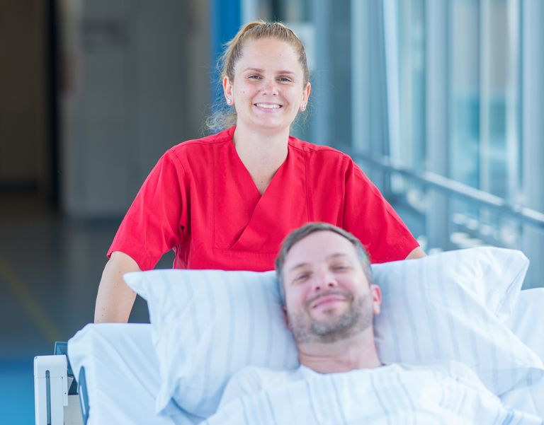 Das Bild zeigt eine Mitarbeiterin des Patientenbegleitservice, die einen Patienten im Bett transportiert