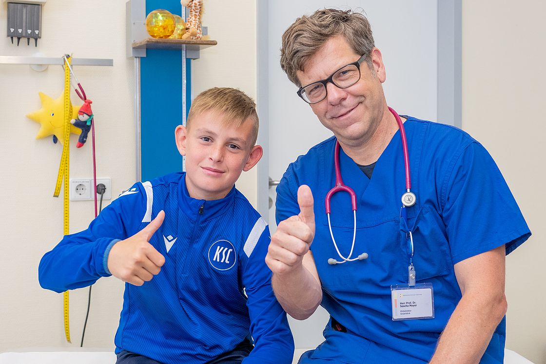 Das Bild zeigt Prof. Meyer und einen Jugendspieler des KSC, den Daumen in die Kamera hebend.