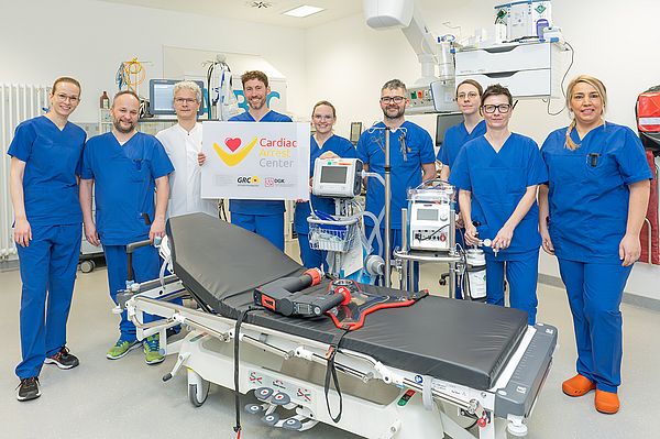 Das Bild zeigt ein Gruppenfoto des ärztlichen und Pflegerischen Teams des Cardiac Arrest Center. Die Personen sehten in blauer Bereichskleidung in einem Schockraum der Zentralen Notaufnahme.