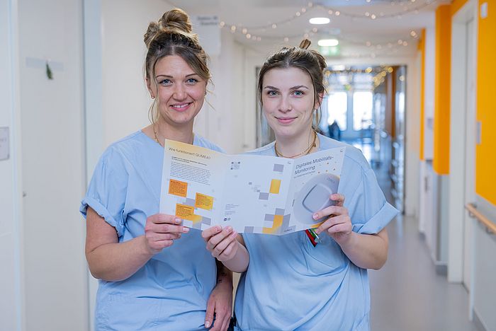 Das Bild zeigt zwei Pflegefachkräfte mit einem Flyer in den Händen.