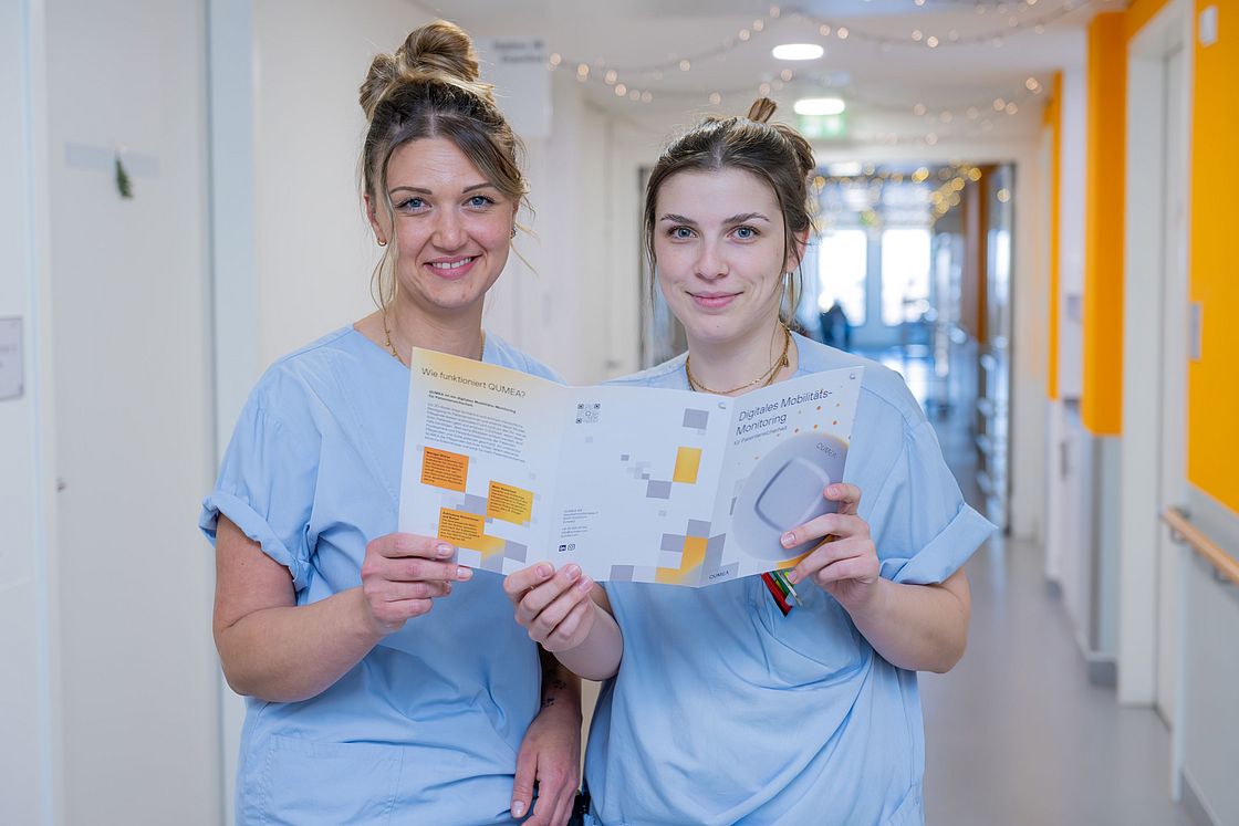 Das Bild zeigt zwei Pflegefachkräfte mit einem Flyer in den Händen.