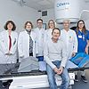 Das Bild zeigt das interdisziplinäre Team um Prof. Katja Lindel (3.v.l.), Prof. Armin Luik (4.v.l.), Dr. Antje Wark (3. v.r.) und Prof. Julian Widder (2.v.r.) mit einem Patienten (sitzend auf dem Linearbeschleuniger).
