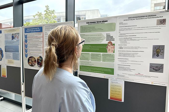 Das Bild zeigt eine Pflegekraft, die wissenschaftliche Plakate betrachtet.