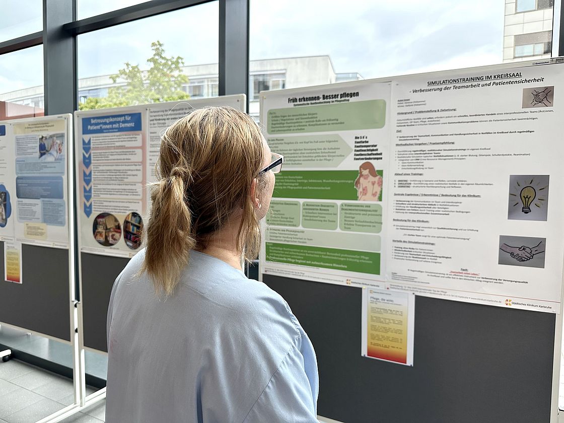 Das Bild zeigt eine Pflegekraft, die wissenschaftliche Plakate betrachtet.