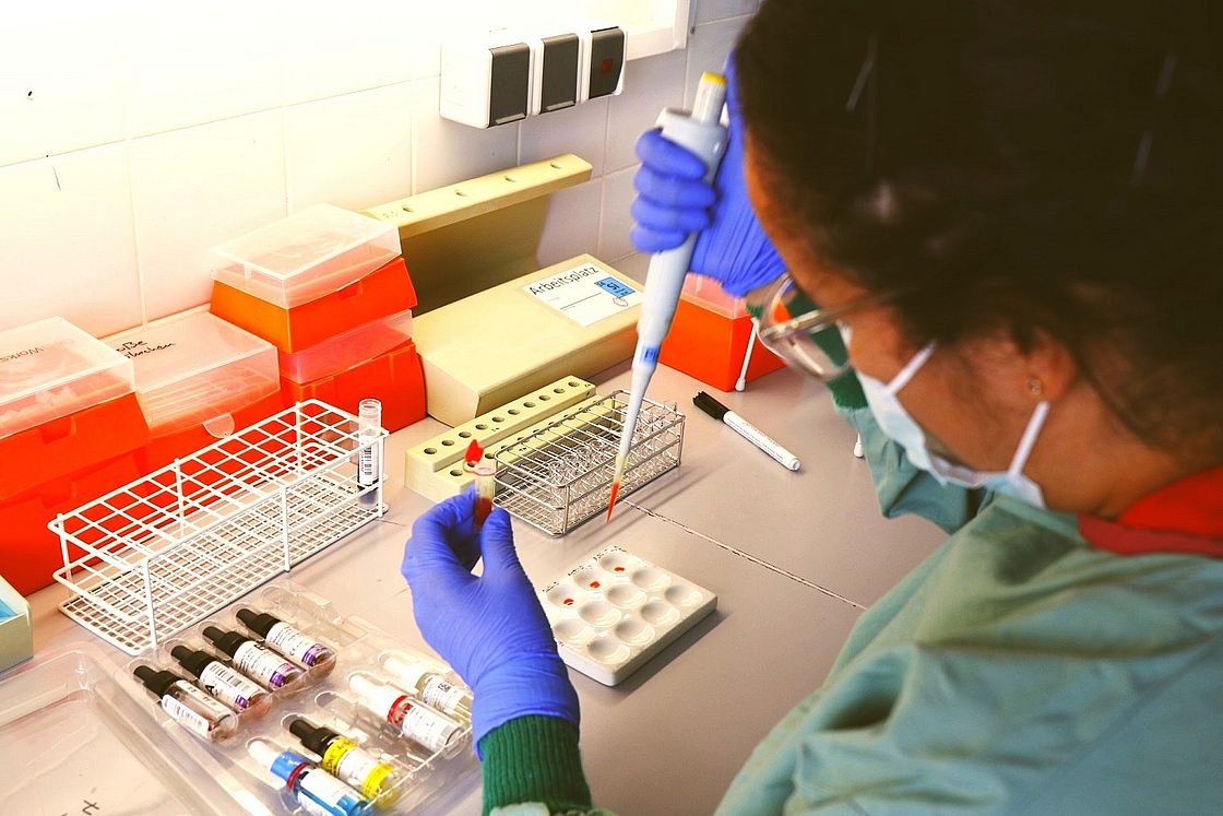 Auf dem Bild sieht man eine Labormitarbeiterin, die mit einer Pipette Blutproben aufbereitet.