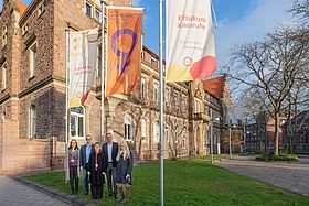 Das Bild zeigt Susanne Trappe-Jost, Prof. Thomas Rüdiger, Claudia Arndt, Markus Heming und Karoline Lanz (v.l.) vor der orangenen Fahne.