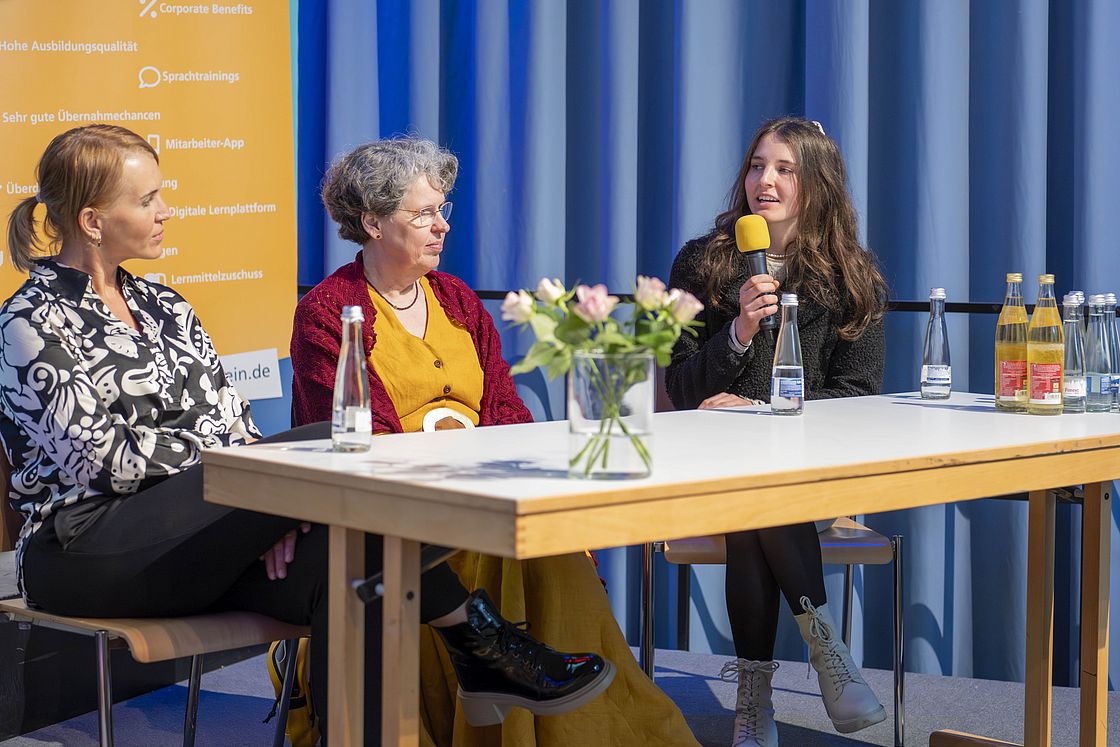 Das Bild zeigt drei Personen bei einer Podiumsdiskussion.