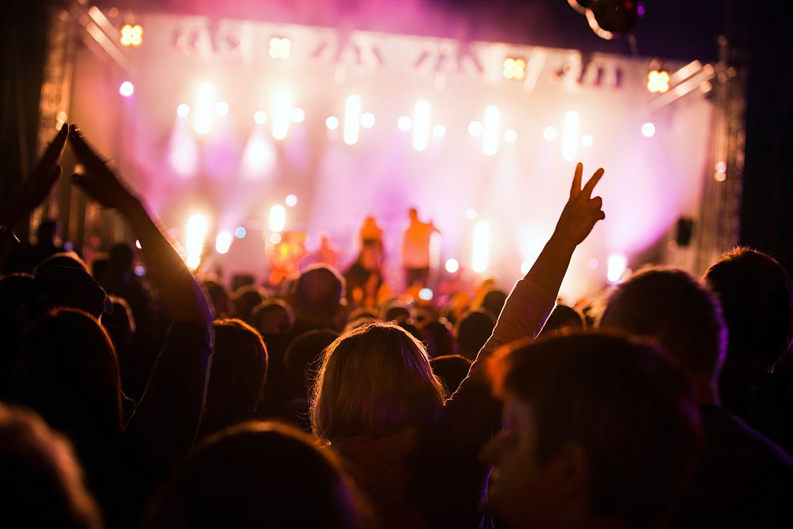Das Foto zeigt Besucherinnen und Besucher, die vor einer Bühne auf einem Musikfestival feiern.