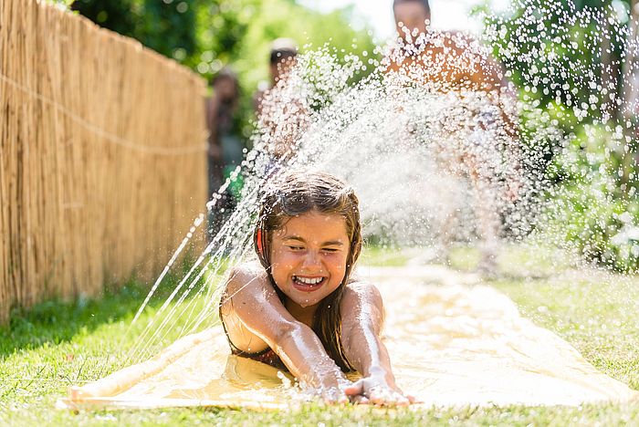 Ein Mädchen kühlt sich an einem Wassersprinkler.