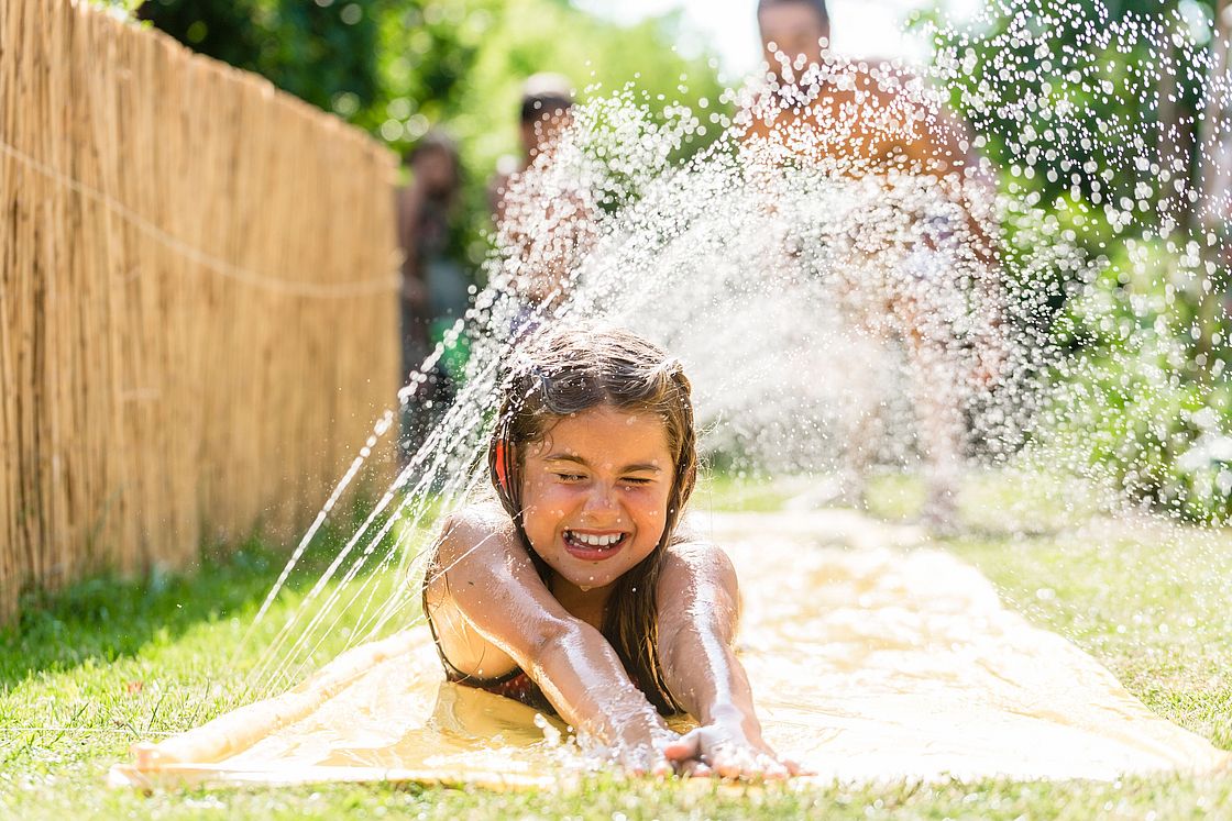 Ein Mädchen kühlt sich an einem Wassersprinkler.